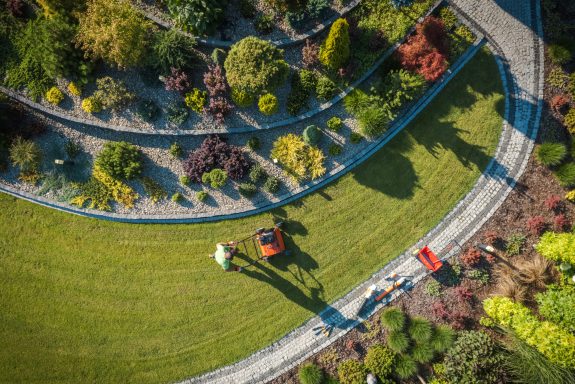 Aerial View of Professional Garden Worker with Push Spreader. Lawn Fertilizing Theme. Gardening and Landscaping Industry.